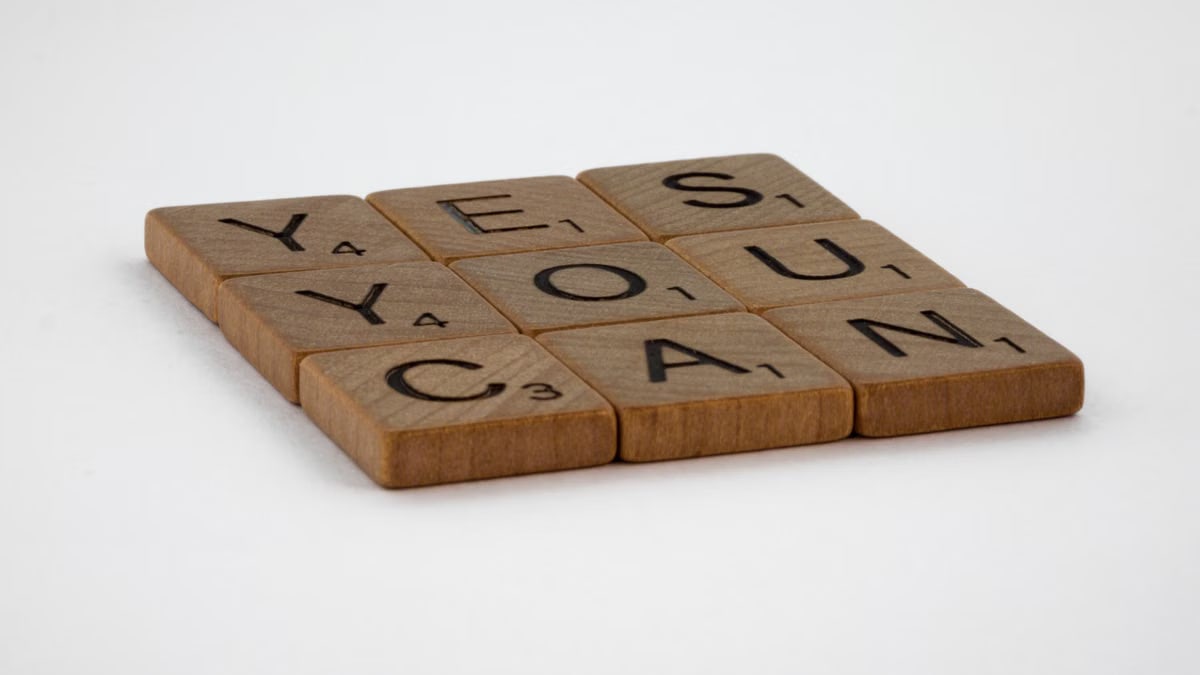 Wooden Scrabble tiles spelling 'Yes You Can' on a white background.